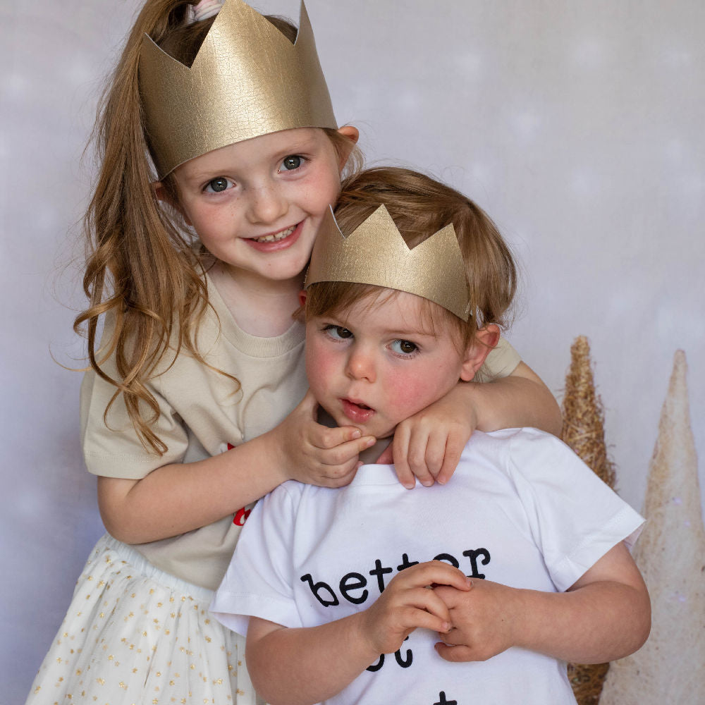 Gold fabric crowns being worn by 2 kids, one a tall classic crown style and the other a mini shorter crown style