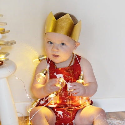 gold christmas crown being worn by a 1 year old boy in a red chrismtas romper and christmas lights for a christmas photo