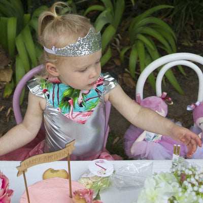 silver birthday crown on a little girl dressed in a silver top and sitting at a table with a birthday cake 