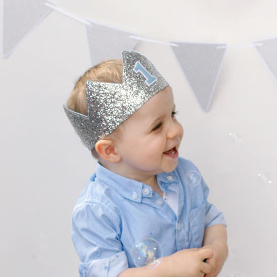 first birthday boy in a silver birthday crown and a blue shirt laughing at bubbles for a first birthday photoshoot