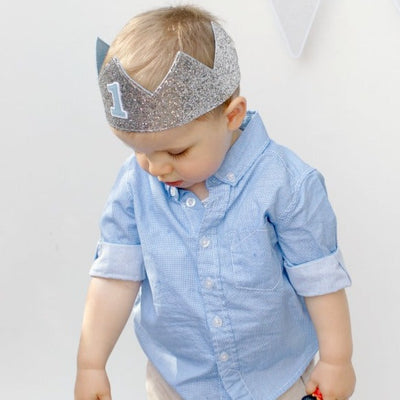 first birthday boy in a silver birthday crown and blue shirt during a 1st birthday photoshoot